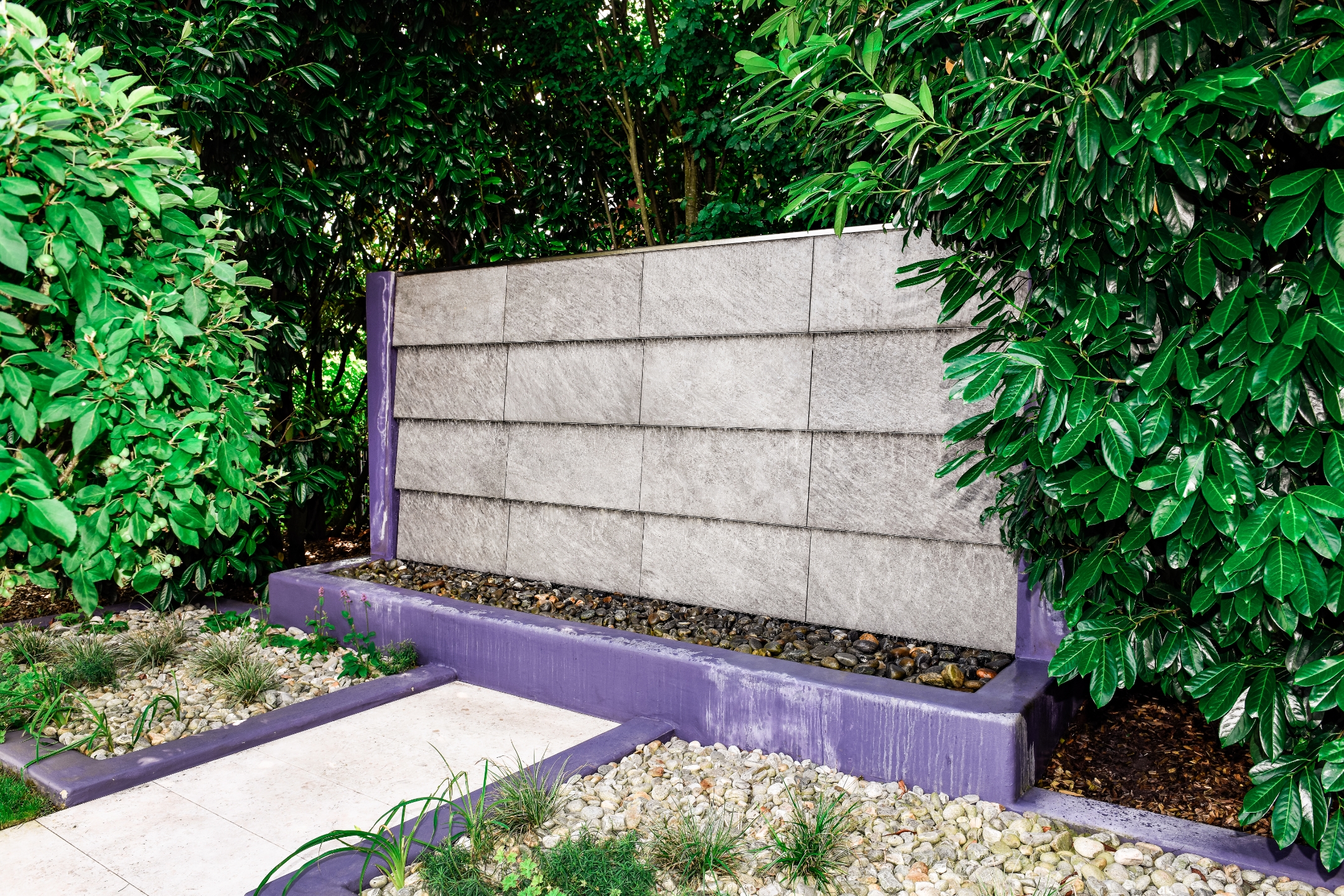 Wasserwand in einem Garten mit lila Sockel