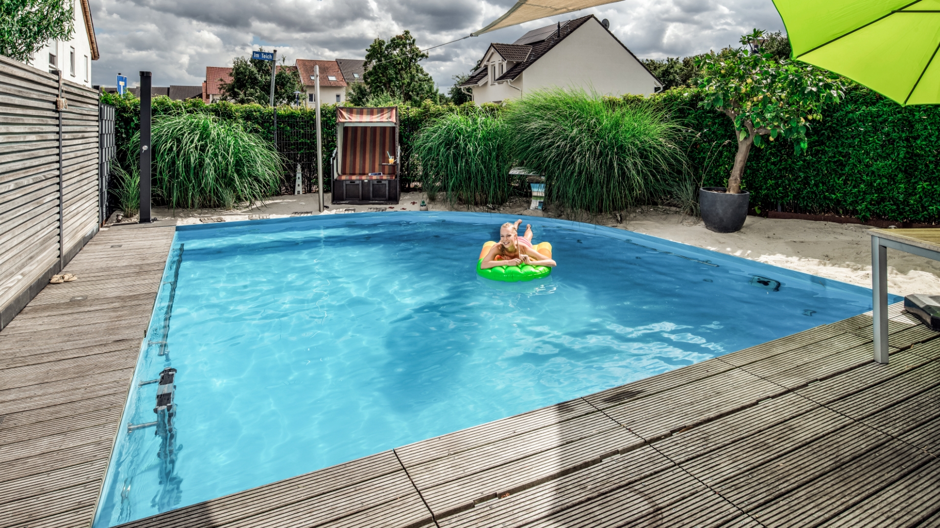 Frau in rosa Bikini springt von links fröhlich ein einen Pool in einem privaten Garten