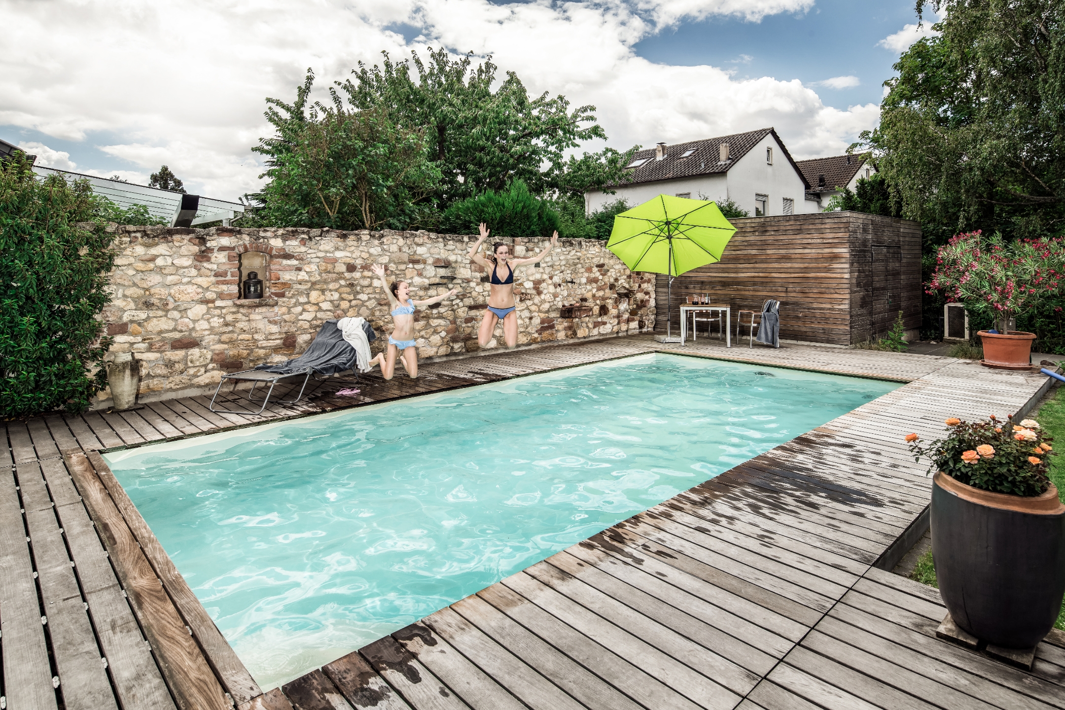 Zwei junge Mädchen im Bikini springen ausgelassen in einen Pool