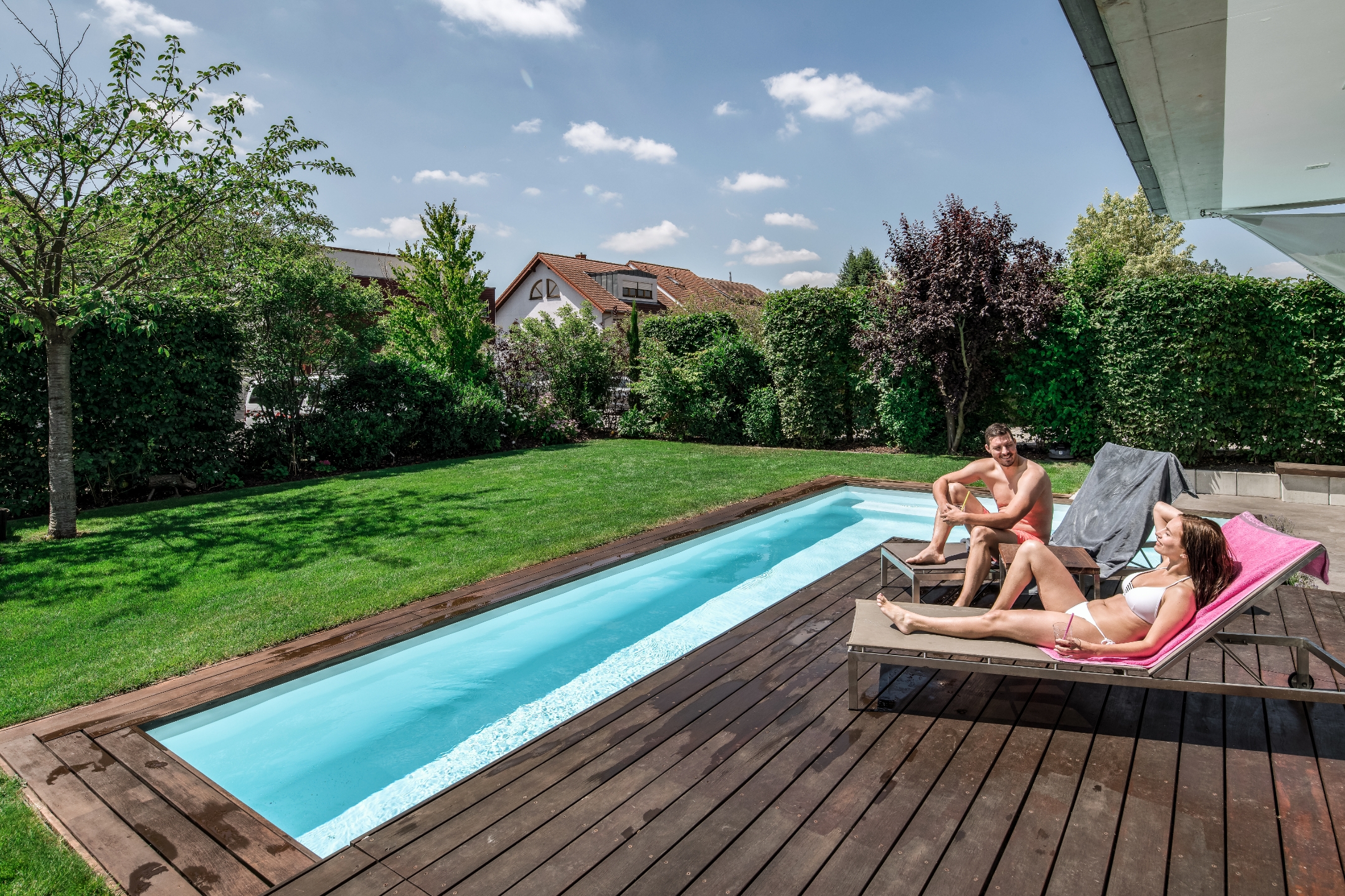 Pärchen sitzt/liegt auf Sonnenliegen auf einer Terrasse, darunter ist ein Pool
