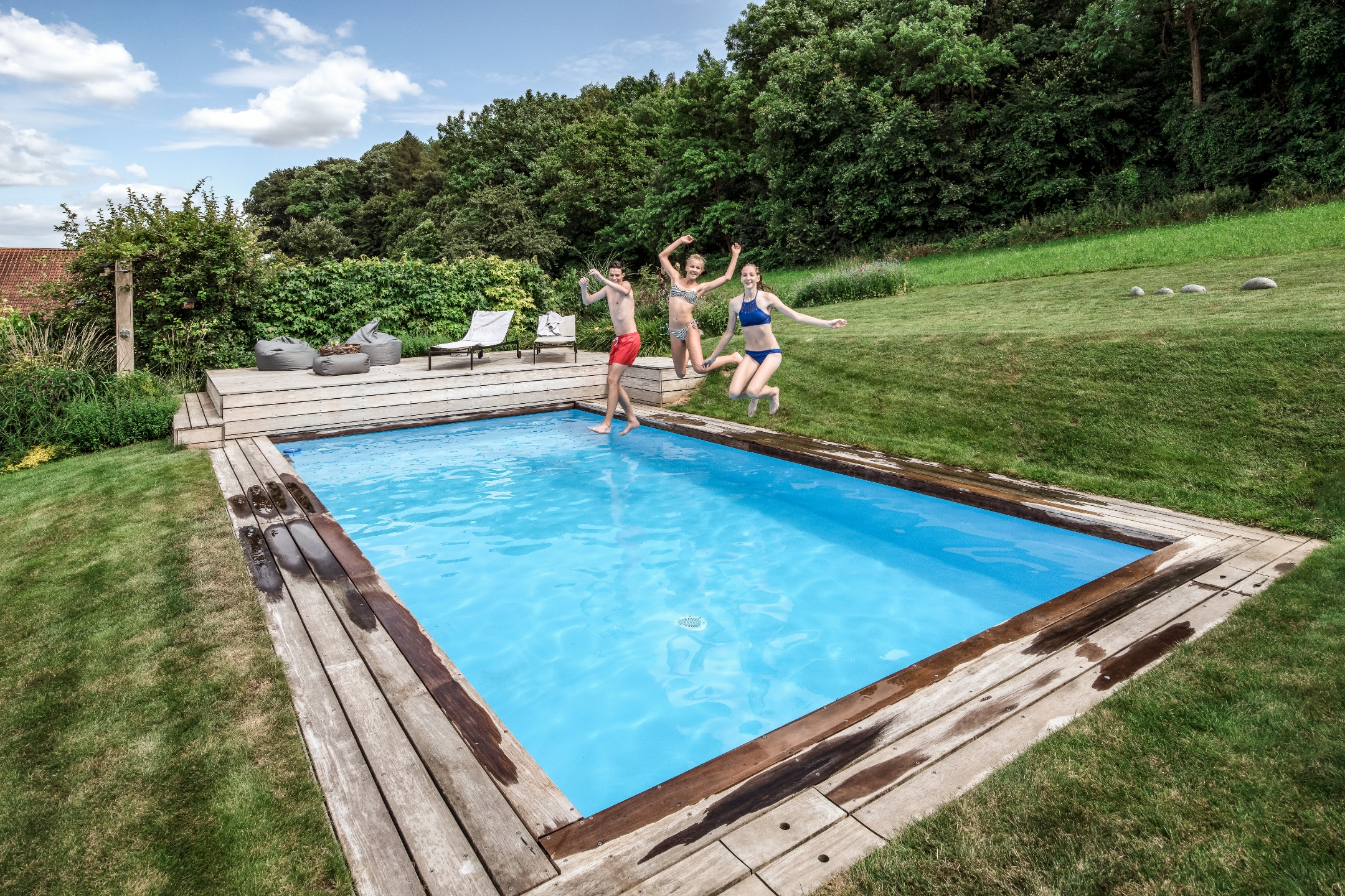 Drei junge Personen hüpfen vergnügt in einen Pool in einem Garten